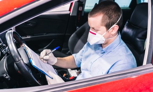 A young caucasian technician doing a security inspection inside a vehicle protected with a mask and gloves to prevent the spread of virus